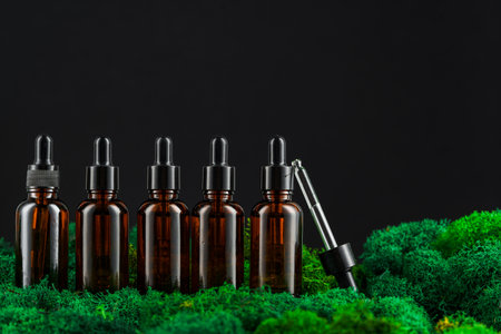 Dark glass bottles arranged in row on green moss against a black backgroundの写真素材
