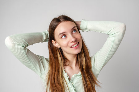 Young Woman With Long Brown Hair Wearing Green Sweater Smiles and Looks Upwardの写真素材