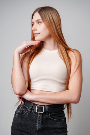 Young Woman Posing In White Crop Top And Black Jeans Against A White Wall
