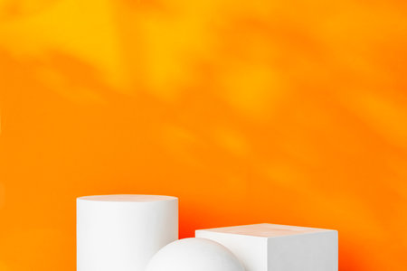 White geometric shapes on a vibrant orange background with soft shadows in a well-lit indoor settingの写真素材