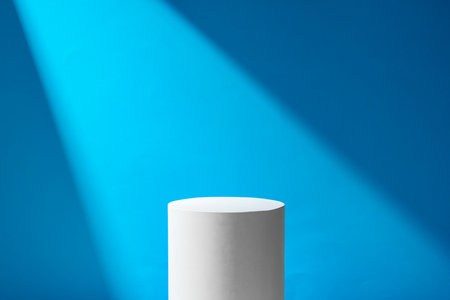 A minimalistic podium illuminated by a beam of light against a blue backdrop in a studio settingの写真素材