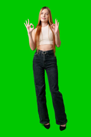 Young Woman With Long Hair Gesturing Okay Sign in Front of Green Screenの写真素材