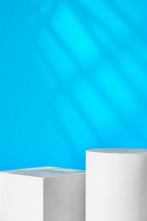 White geometric shapes on a clean surface against a bright blue background with soft shadowsの写真素材