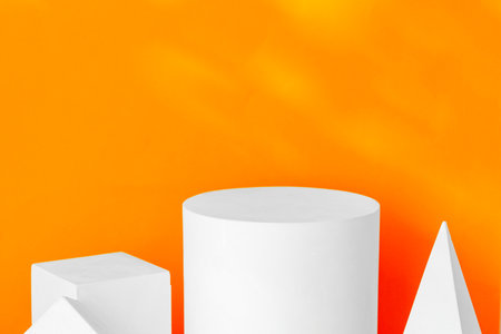 White geometric shapes on a vibrant orange background with soft shadows in a well-lit indoor settingの写真素材