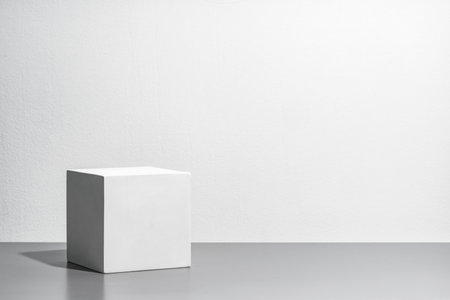 A simple white cube on a gray surface against a blank wallの写真素材