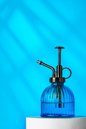 A blue misting spray bottle on a white pedestal against a bright blue backgroundの写真素材