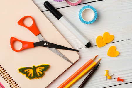 Colorful stationery arrangement with a butterfly sticker on a blank notebook at a wooden table in natural lightの写真素材
