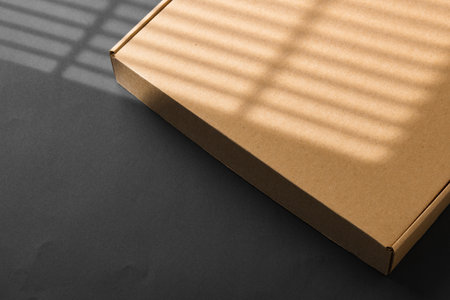 A cardboard box casting shadows on a dark surface in a striped light patternの写真素材