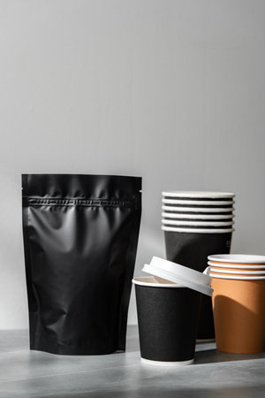 Pouch and stacked disposable cups on a gray surface in a cafe setting during the dayの写真素材
