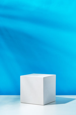 A clean white cube positioned on a minimalist surface against a vibrant blue backdropの写真素材
