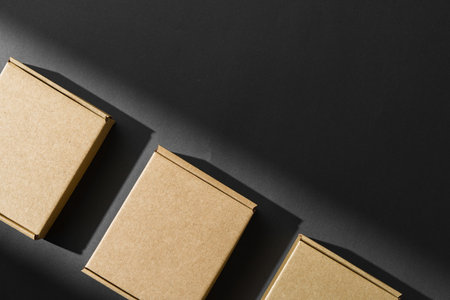 Various sizes of brown cardboard boxes arranged on a black surface with soft lighting effects during the dayの写真素材