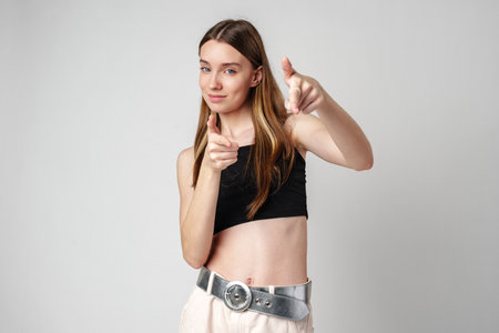 Young Woman in Black Crop Top and Beige Pants Points at the Cameraの写真素材