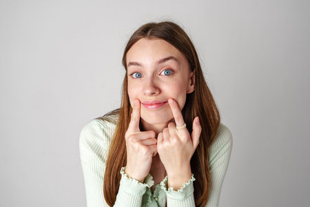 Young Woman With Long Brown Hair Smiles and Touches Her Cheeksの写真素材