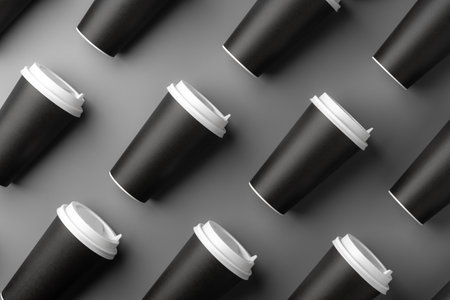 Black disposable cups arranged on a gray surface with white lids, creating a look suitable for a coffee shop settingの写真素材