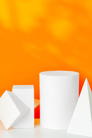 White geometric shapes on a vibrant orange background with soft shadows in a well-lit indoor settingの写真素材