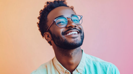 A young man smiles brightly against a colorful, blurred pink and orange backdrop, capturing a moment of joy and positivityの素材