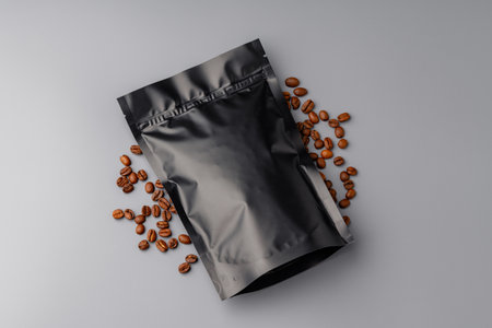 A bag of premium coffee beans surrounded by scattered coffee beans on a gray backgroundの写真素材