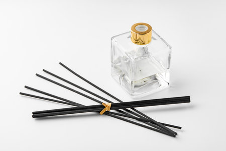A minimalist display of essential oil and black diffuser sticks on a clean white background