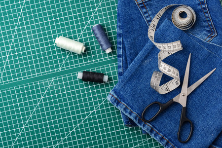 Sewing tools on a cutting mat with denim and thread spools in a craft workspace