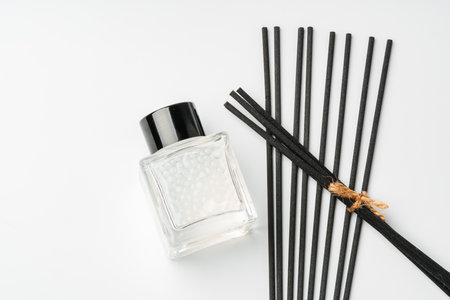 A minimalist display of essential oil and black diffuser sticks on a clean white background