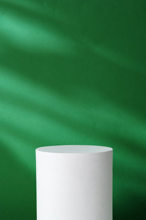 Plain white cylindrical pedestal against a green background with soft shadows in a bright interior settingの写真素材