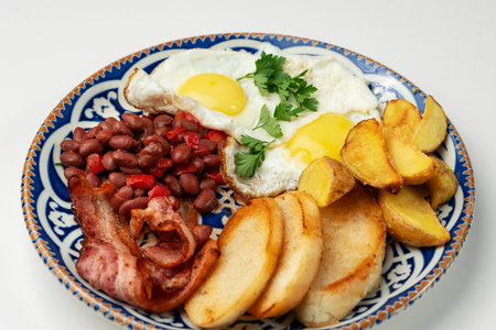 Delicious breakfast plate featuring eggs, beans, bacon, and potato wedges served on a decorative dishの写真素材