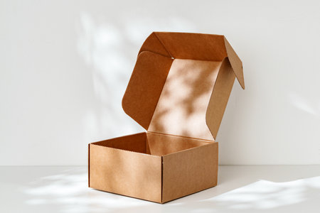 An open cardboard box rests on a bright white surface with soft shadows highlighting its edges and...
