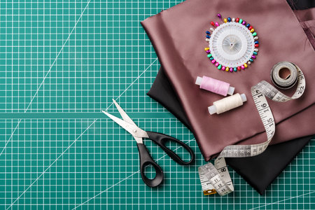 Craft supplies for sewing on a green cutting mat with fabric, scissors, and measuring tools