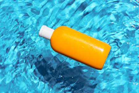 Sunscreen bottle floating in a clear blue swimming pool on a sunny dayの写真素材