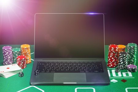 A laptop and poker chips arranged on a green felt table in an indoor gaming setup during a nighttime gambling sessionの写真素材