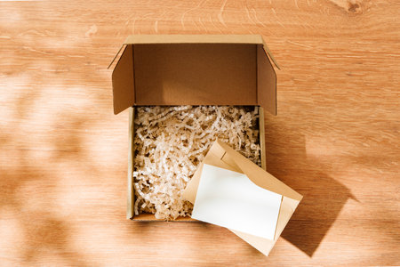 Open cardboard box filled with shredded paper and a blank card on a wooden surface