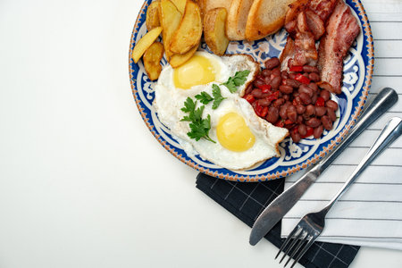 Delicious breakfast plate featuring eggs, beans, bacon, and potato wedges served on a decorative...