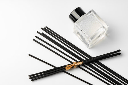A minimalist display of essential oil and black diffuser sticks on a clean white background