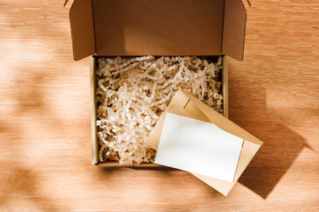 Open cardboard box filled with shredded paper and a blank card on a wooden surfaceの写真素材