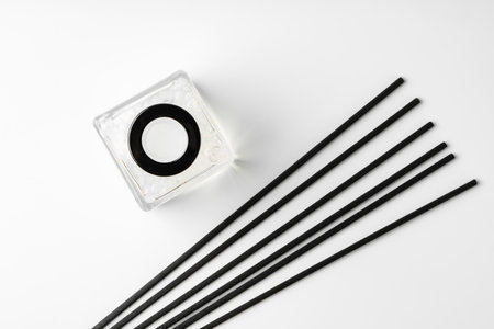 A minimalist display of essential oil and black diffuser sticks on a clean white background