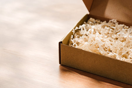 Open cardboard box with shredded paper filling on a wooden table