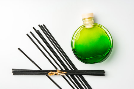 A minimalist display of essential oil and black diffuser sticks on a clean white background