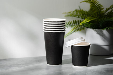 Stack of disposable cups beside a potted plant on a marble surface in natural lightの写真素材