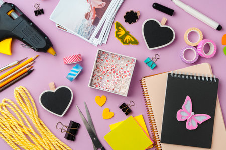 Crafting supplies arranged on a pink background, including glue gun, scissors, and decorative items for DIY projectsの写真素材
