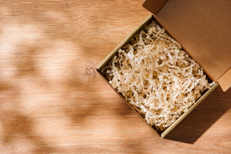 Open cardboard box with shredded paper filling on a wooden tableの写真素材