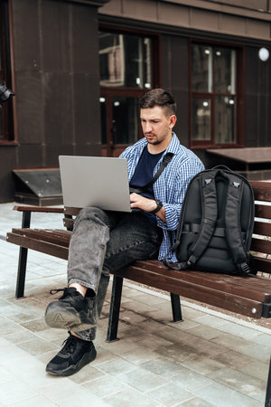 Young man working on a laptop while seated on a bench outsideの写真素材