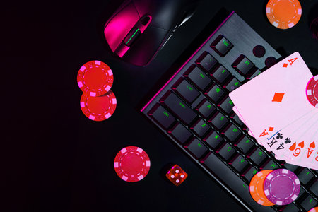 A vibrant arrangement of poker chips and playing cards on a gaming keyboard with a mouse at an online casino setup during the eveningの写真素材