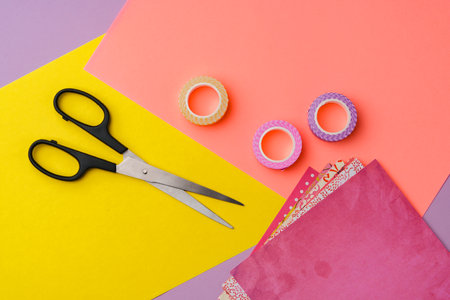 Scissors and decorative tape on colorful craft paper in a bright workspace