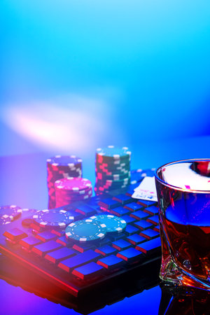 A vibrant arrangement of poker chips and playing cards on a gaming keyboard with a mouse at an online casino setup during the eveningの写真素材