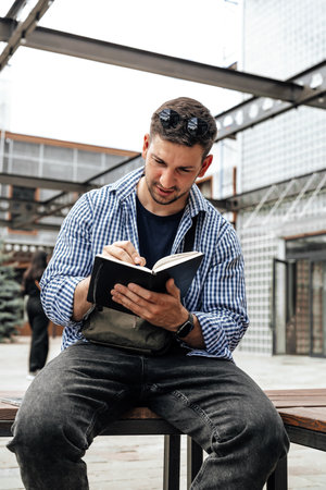 A person writes in a notebook while sitting on a park bench