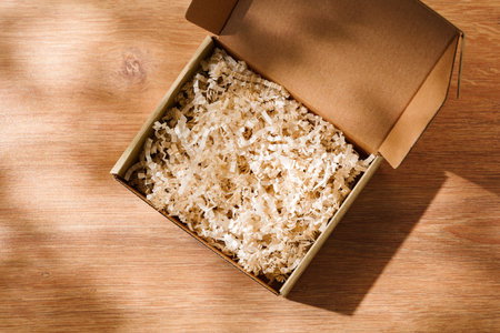 Open cardboard box with shredded paper filling on a wooden tableの写真素材