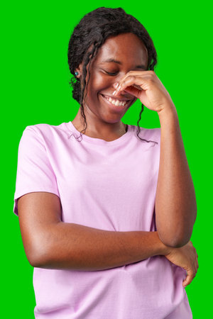 Happy young person laughing and playfully covering face while standing against a bright green backgroundの写真素材