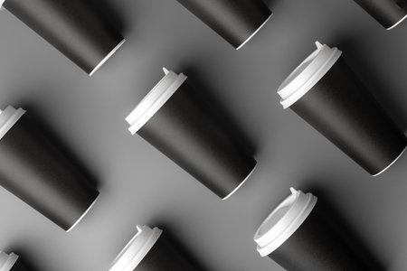 Black disposable cups arranged on a gray surface with white lids, creating a look suitable for a coffee shop settingの写真素材