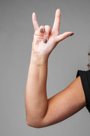 A person making the I love you gesture with their hand in front of a neutral gray backgroundの写真素材