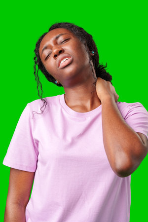 Young woman experiencing neck pain against a bright green backgroundの写真素材